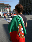 Manifestante com a bandeira portuguesa frente à praça e o Banco Nacional Suíço.